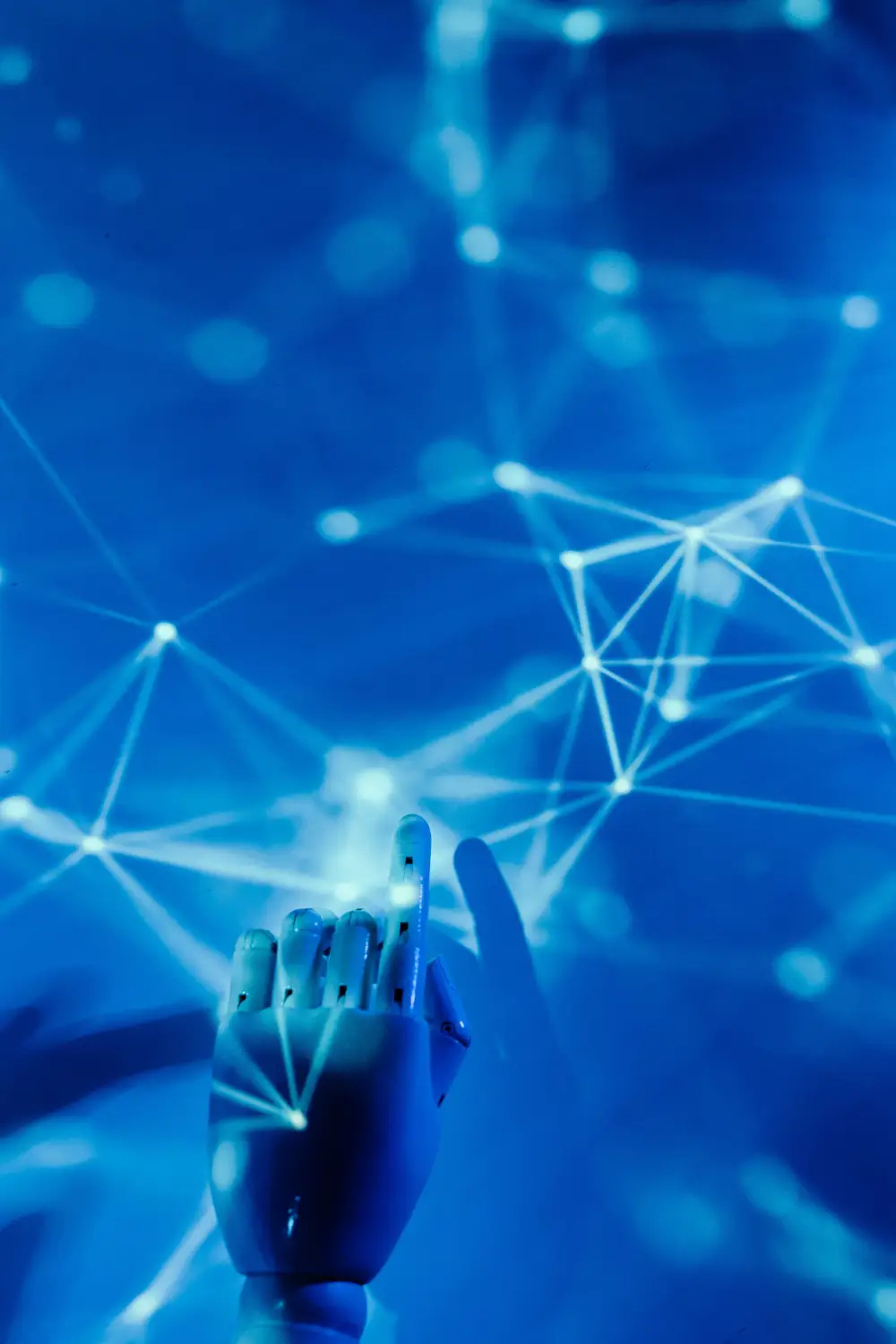 humanoid-robot-hand-neural-network A humanoid robot hand pointing upward toward an abstract, glowing blue neural network diagram made of interconnected data nodes and lines.