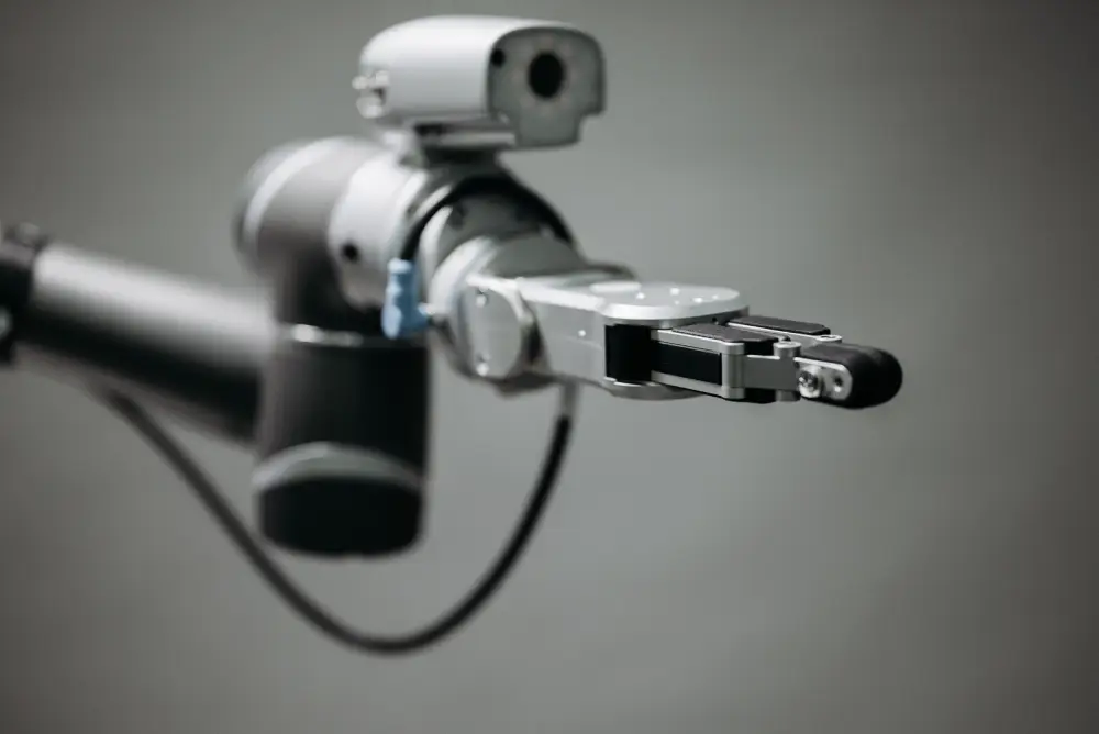 robotic-arm-gripper-close-up A close-up shot of a modern industrial robotic arm featuring a precise two-finger gripper end-effector against a neutral grey background.